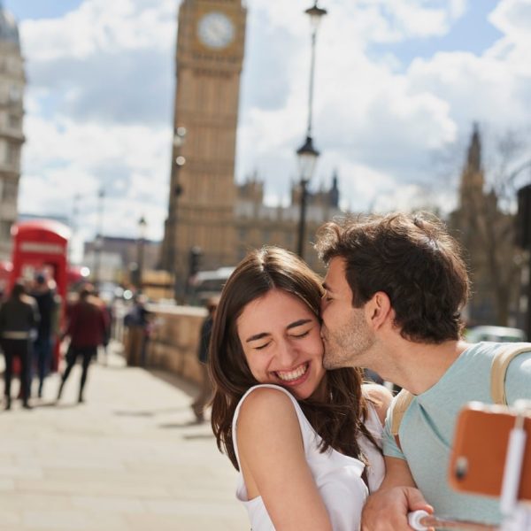 Natalia De La Pena London.jpg, Juan Carlos Ortega London.jpg Couple, travel and selfie with kiss outdoor in London for romantic holiday, adventure and love in city street. Man, woman and smartphone, happiness with smile in traveling photo, tourist and romance